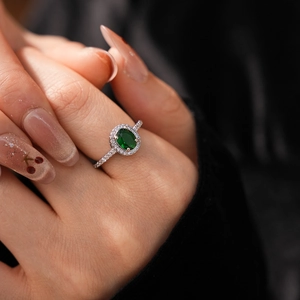 Detailed close-up of oval green gemstone ring with halo diamonds on a silver band