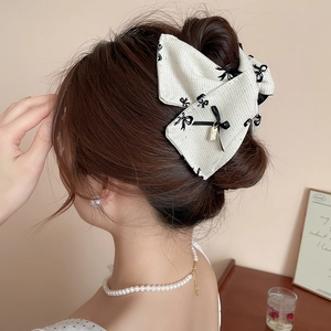 Detailed side view of an ivory bow hair claw clip styled on a woman's hair in a cozy setting