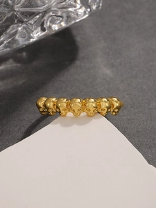 Dettaglio di anello teschio dorato vintage con teschi multipli continui su sfondo minimalista