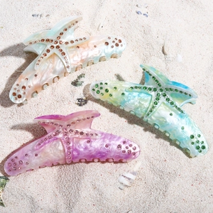 Close-up of three starfish hair claws with rhinestones on a sandy beach background