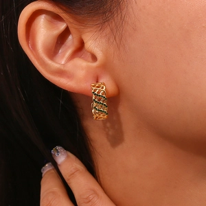 Vue macro de boucles d'oreilles dorées avec maille tressée et pierres vertes