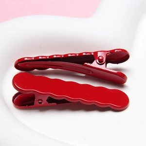 Detail of red wavy hair clips showing glossy finish and duckbill clamp mechanism