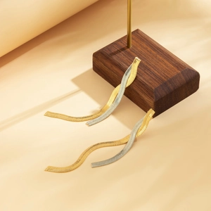 Close-up of elegant two-tone snake chain tassel earrings on a premium wooden display stand