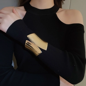 Close-up of a wide irregular gold cuff bracelet worn over a black sleeve in a luxury style