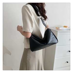 Detailed view of a large black leather tote bag worn by a model in a minimalist setting