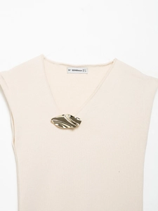 Close-up detail of beige ribbed knit V-neck top featuring a gold wavy brooch and brand tag