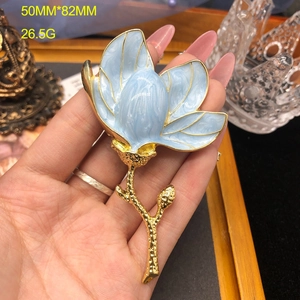 Detail view of a blue enamel magnolia brooch with gold trim measuring 50mm by 82mm