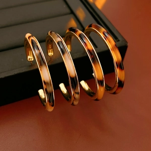 Close-up of C-shaped leopard print resin earrings with golden metal on a brown leather surface