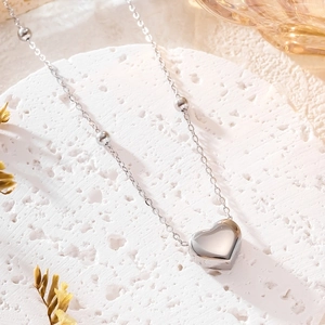 Detailed view of silver heart pendant on a bead chain over a textured white stand