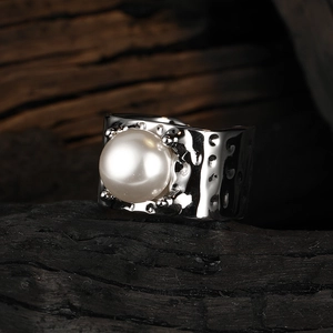 Macro shot of wide silver textured ring featuring a central white pearl on wood background