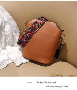 Detail of brown PU leather bucket bag with ethnic style wide shoulder strap on beige sofa