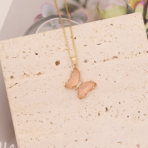 Détail d'un collier papillon doré avec ailes en résine rose et strass sur pierre
