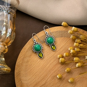 Detailed shot of retro silver earrings with turquoise and olive teardrop stone on wood
