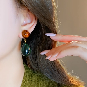 Asymmetrical drop earrings with amber studs and dark green resin pendants on model