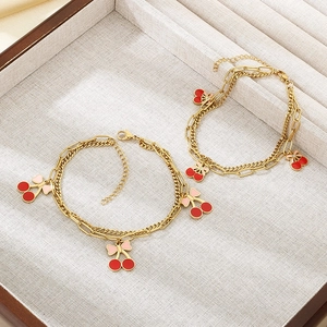 Detail of 18K gold-plated layered anklets with red cherry and bow pendants on tray