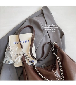 Detail of dark brown leather handbag with adjustable strap and metal chain on a blazer