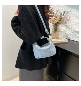 Detail of light blue crossbody bag with denim texture and metallic hardware on shoulder strap