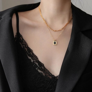 Detail of layered gold chunky chain and minimalist black square pendant on a model