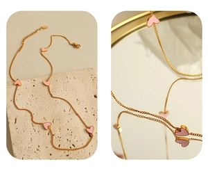 Detail of gold necklace with five pink heart charms on a natural stone surface