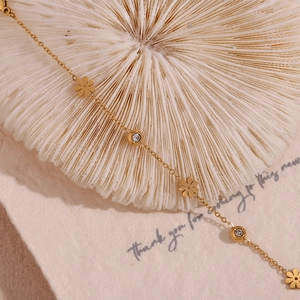 Detail of 18K gold daisy bracelet with zircon charms on white textured background