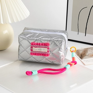 Détail de la trousse de maquillage argentée matelassée avec étiquette rose et zip tressé