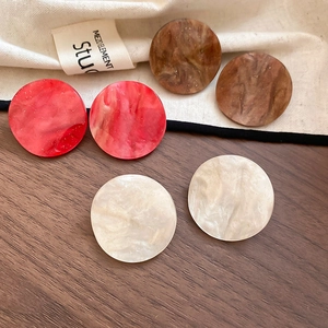 Detail view of three pairs of acrylic round stud earrings with marble patterns and gold glitter