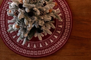 Detail of red knit Christmas tree skirt with white snowflake patterns on wood floor