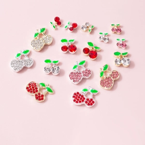 Detailed view of cherry-shaped 3D nail art charms with rhinestones on a pink background
