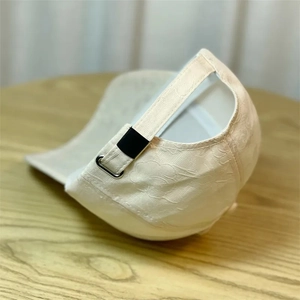Detail of cream baseball cap featuring textured floral fabric and a black metal buckle