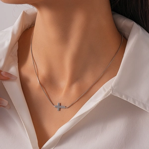 Close-up of polished silver cross pendant on box chain worn with a white shirt