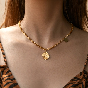 Close-up of gold chain necklace with wavy textured square pendant on model neck