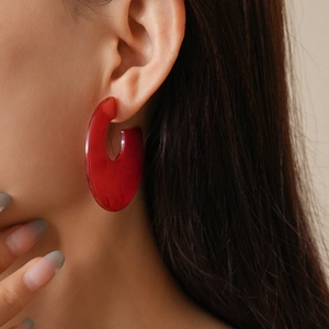 Close-up of a large red C-shaped acrylic earring worn by a model in a trendy style