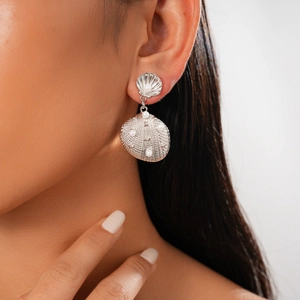 Close-up of silver shell earrings with white pearls and textured metal on a model