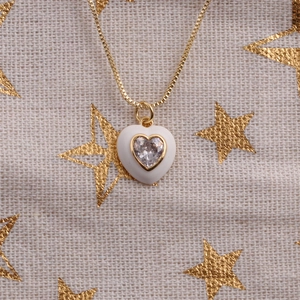 Close-up of a gold heart pendant with white enamel inlay and central clear zircon stone