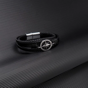 Detail of hand-woven black leather bracelet for men featuring a silver compass magnetic clasp