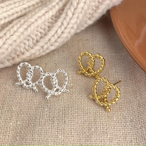 Detail view of twisted rope knot stud earrings in gold and silver on linen fabric
