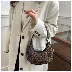 Detail of leopard print crescent bag with black strap worn with a beige blazer