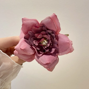 Pink and deep purple fabric flower hair claw clip held in hand against beige background