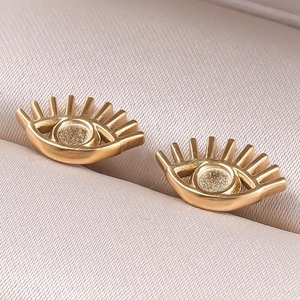 Detailed close-up of gold-tone eye-shaped stud earrings with intricate eyelash textures