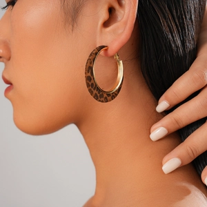 Close-up of leopard print velvet hoop earrings with gold metal trim on model