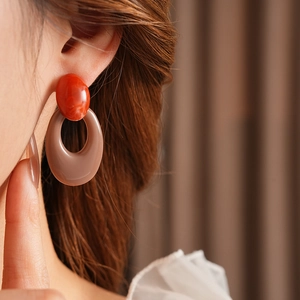 Close-up of retro oval acrylic drop earrings in orange and brown on model
