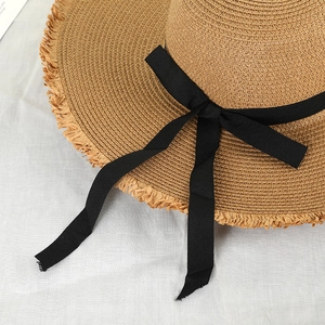 Close-up of straw sun hat with black ribbon bow and stylish frayed raw edge texture