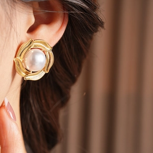 Detailed close-up of retro pearl stud earrings with golden spiral texture design