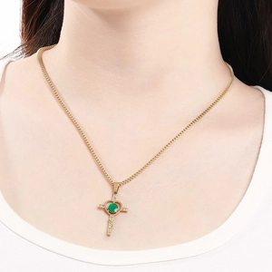 Detail of gold cross heart necklace featuring a green gemstone and sparkling crystals