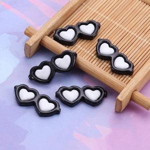 Detail of five mini heart-shaped black sunglasses resin accessories on bamboo mat