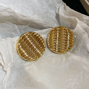 Detail of round golden ripple textured acrylic earrings on white textured background