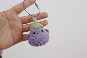 Detailed view of a handmade crochet eggplant keychain with green leaves and a purple cord