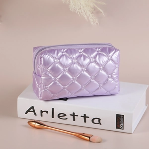 Purple quilted diamond pattern cosmetic bag with glossy finish on a decorative book