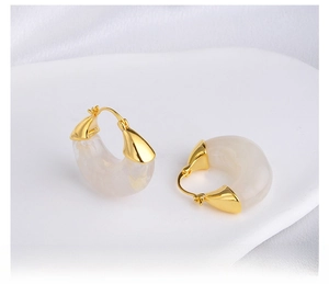 Detail of C-shaped gold metal and milky white marble resin earrings on silk background