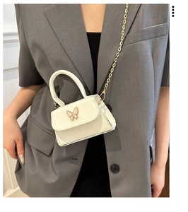 Détail du mini sac blanc avec boucle papillon dorée et bandoulière en chaîne